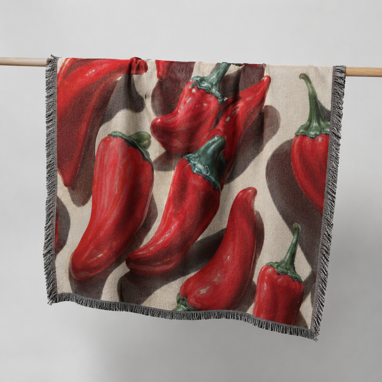 Blanket with red chili pepper pattern draped over a wooden rod on a light gray background